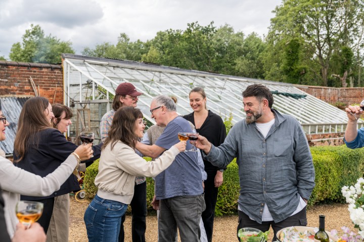 Group of people toasting with drinks outside near a greenhouse.