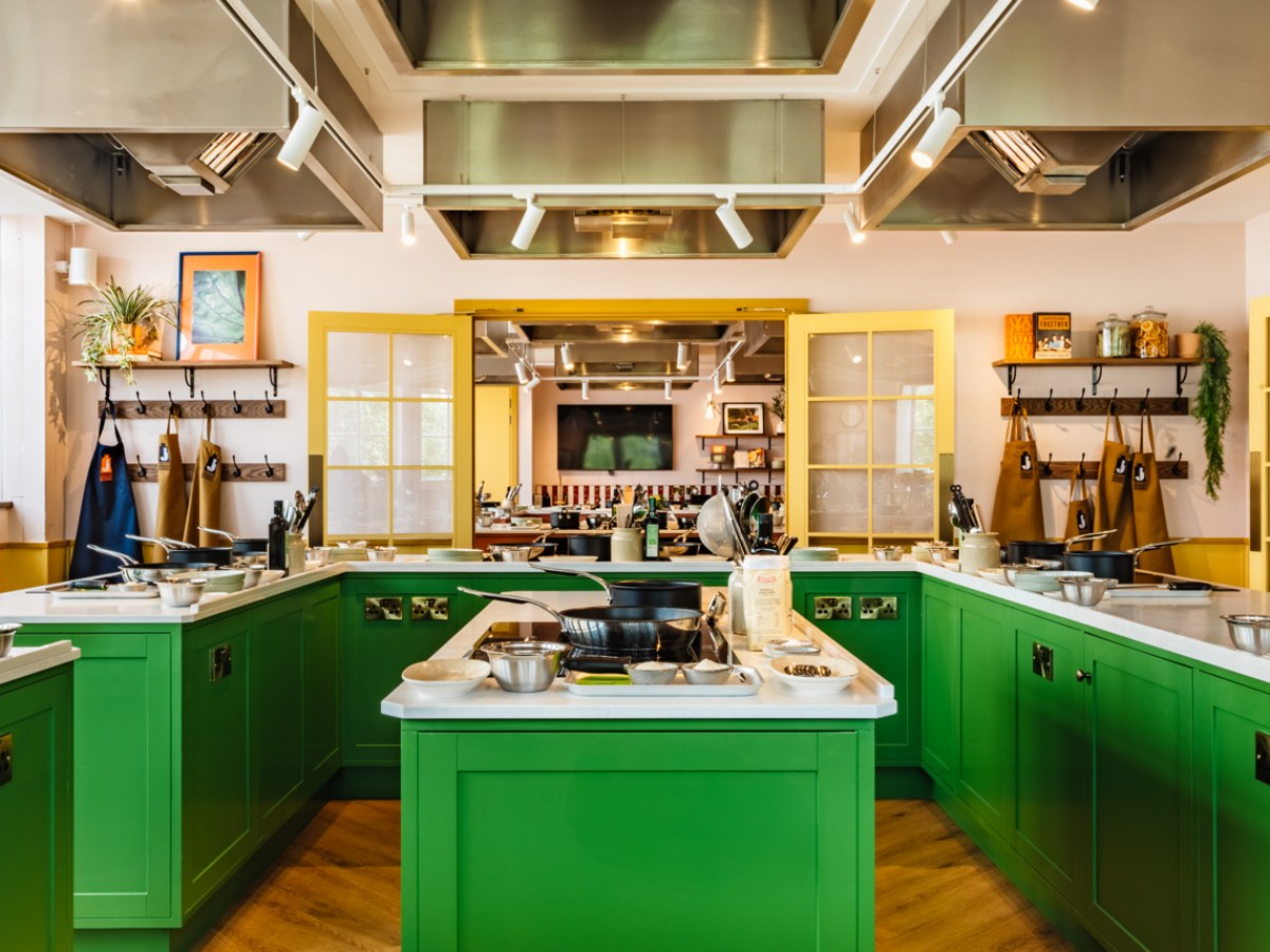 Modern kitchen with green cabinets, cooking tools, and aprons on racks.