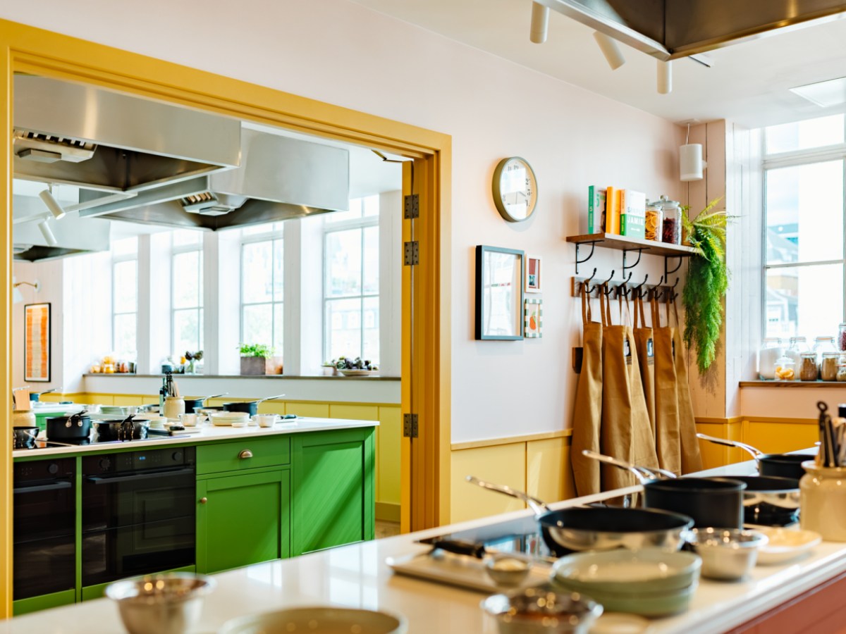 Modern kitchen with green cabinets, aprons on hooks, and cookware on counters.