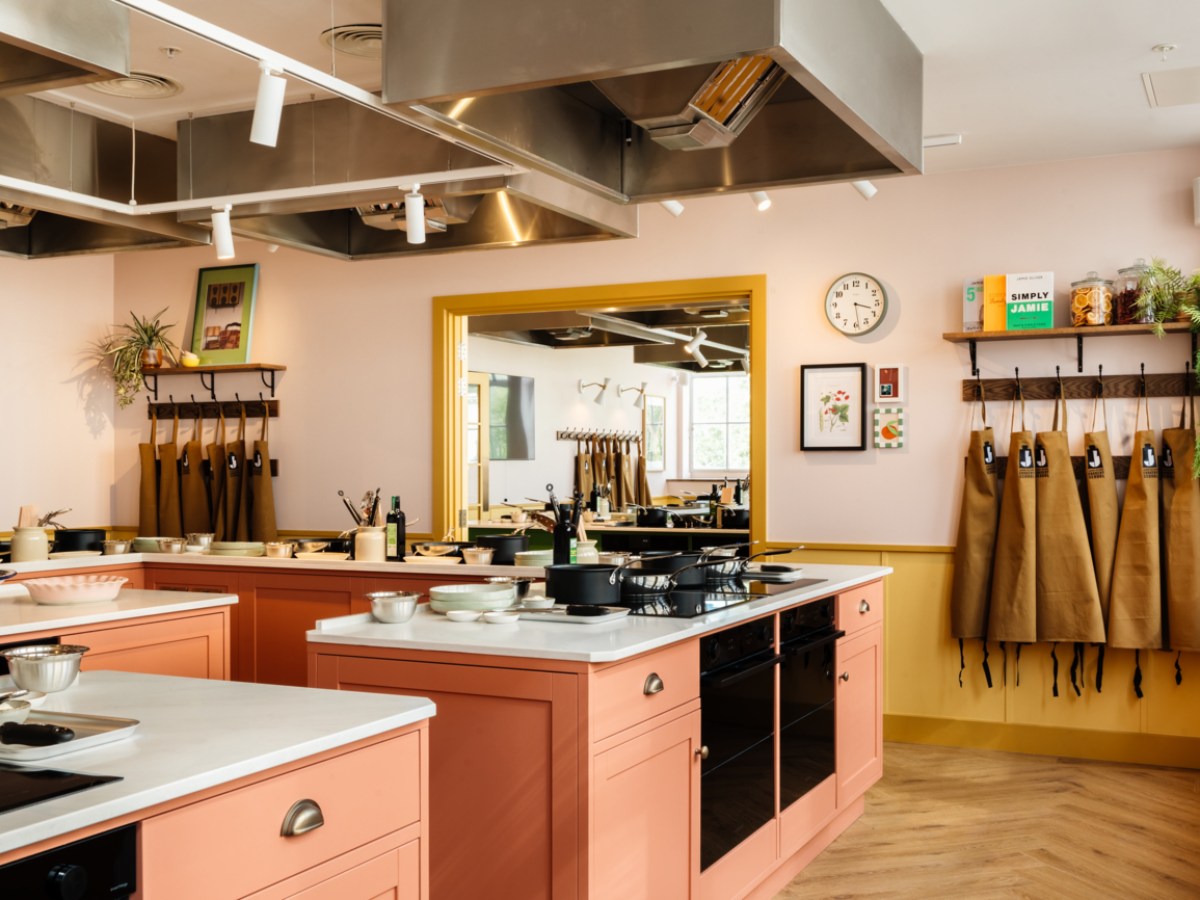 Modern kitchen with pink cabinets, utensils, aprons hanging, and a large mirror on the wall.