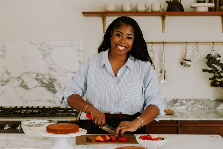 Person slicing strawberries in a kitchen with cakes and a marble countertop.