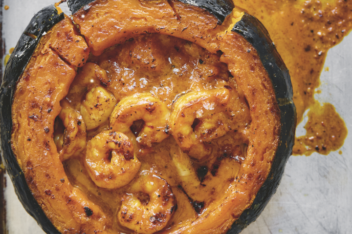 Roasted stuffed pumpkin with shrimp on a baking sheet, lid set aside.