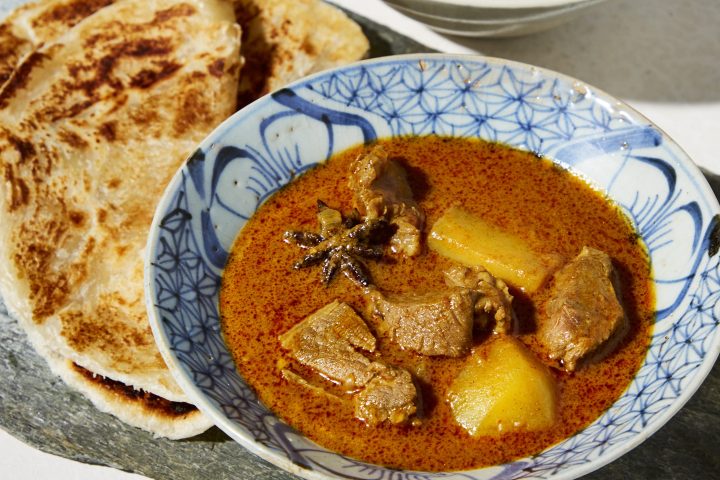 Two bowls of curry with meat and potato, served with flatbread on slate.