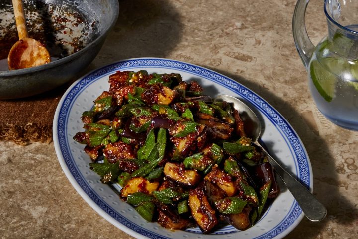 Colorful vegetable stir-fry on a blue-patterned plate next to an empty pan and glass pitcher with lime water.