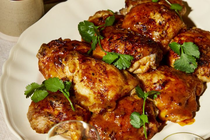 Plate of glazed chicken with herbs, wine glasses, and sauce bowl.