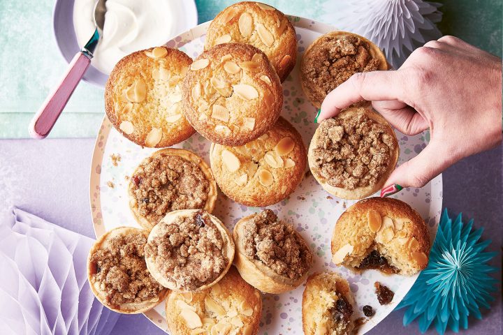 Hand picking a crumbly muffin from a platter with decorations and a bowl of cream nearby.