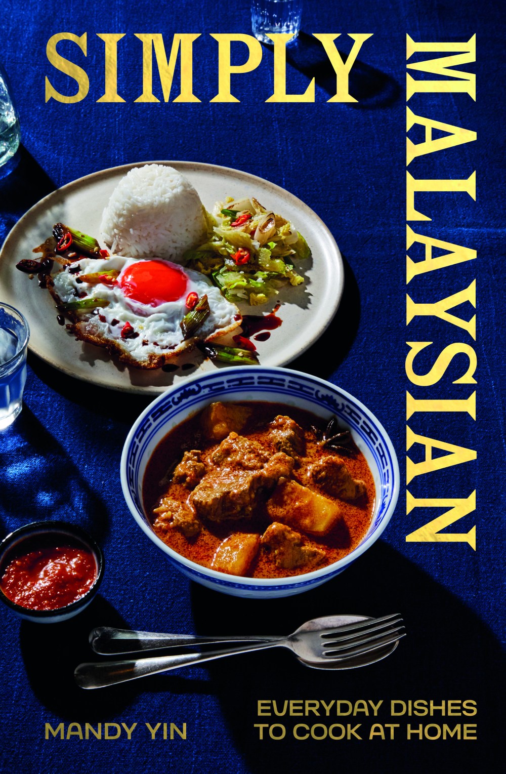 Book cover with Malaysian dishes: rice, egg, vegetables, curry in blue bowl on a blue tablecloth.