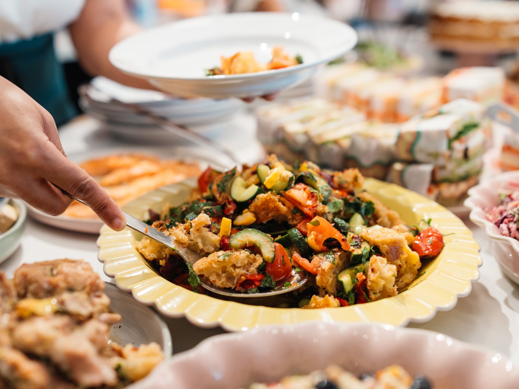 A person serves vegetable salad from a buffet table with various dishes.