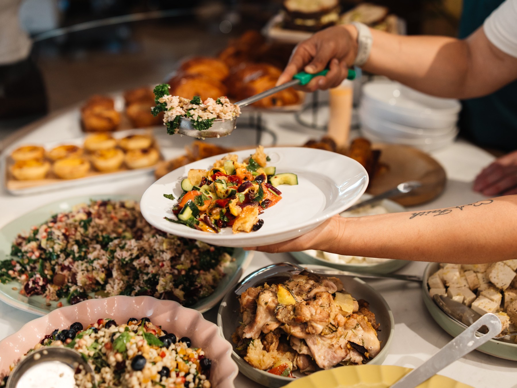 Person serving food onto a plate at a buffet with various dishes.