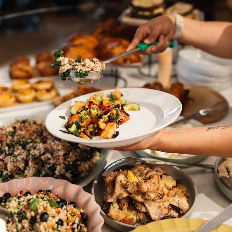 Person serving food onto a plate at a buffet with various dishes.