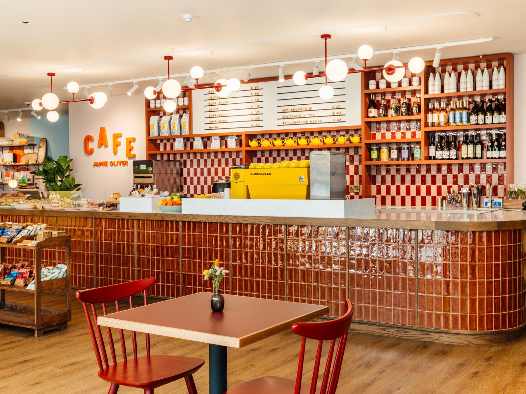 Cozy café interior with red tiles, wooden furniture, and illuminated signs on the wall.