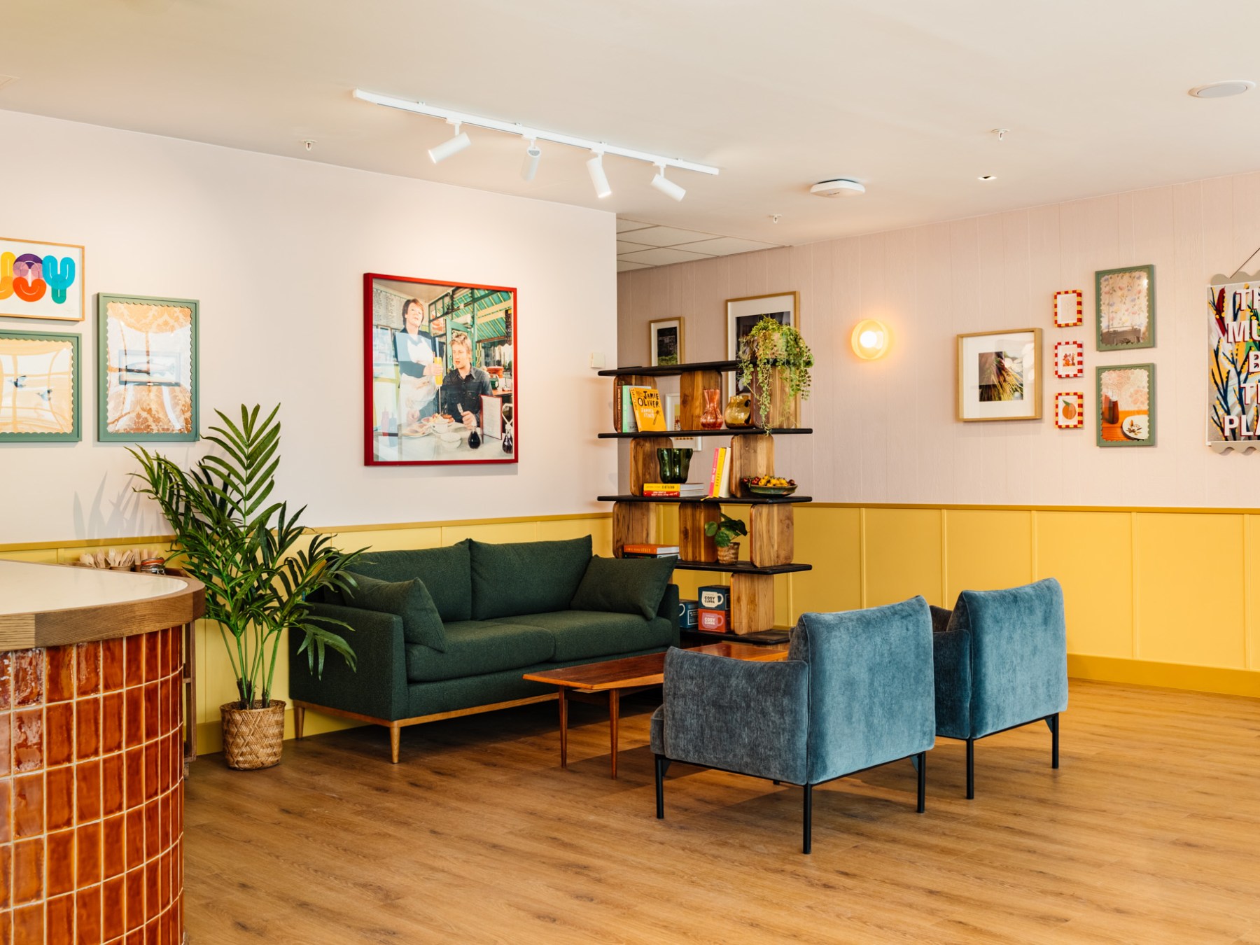 Stylish lounge with green sofa, two blue chairs, and various colorful artworks on pastel walls.