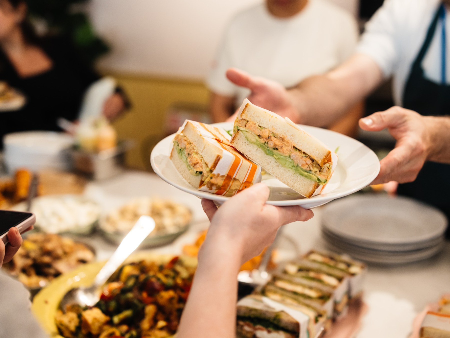 Person holding a plate with sandwich slices at a buffet with people in the background.