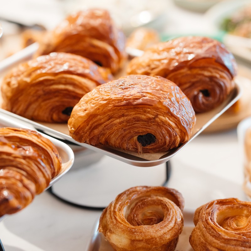 Close-up of trays with assorted pastries, including croissants and swirls, on a table.