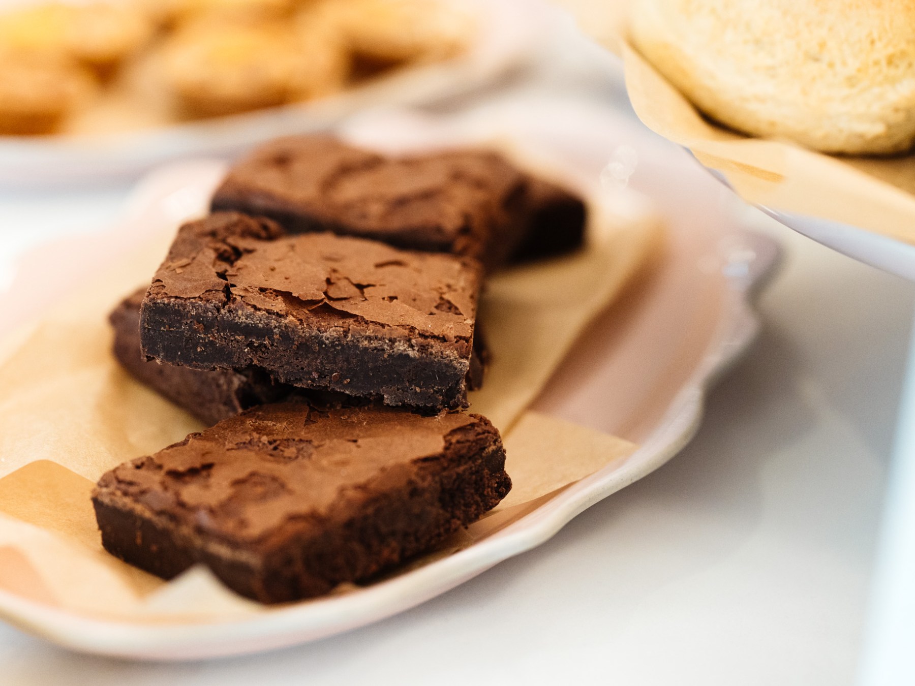 Close-up of chocolate brownies on a white plate with other pastries in the background.