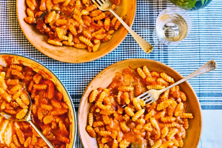 Three plates of pasta with tomato sauce on a checkered tablecloth.
