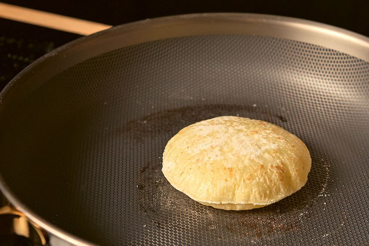 Round bread cooking in a non-stick frying pan on stovetop.