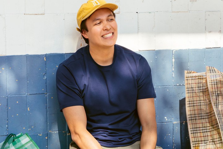 Smiling person in yellow cap sitting by blue and white wall.
