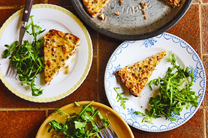 Three plates with potato cake slices and arugula on a tiled surface.