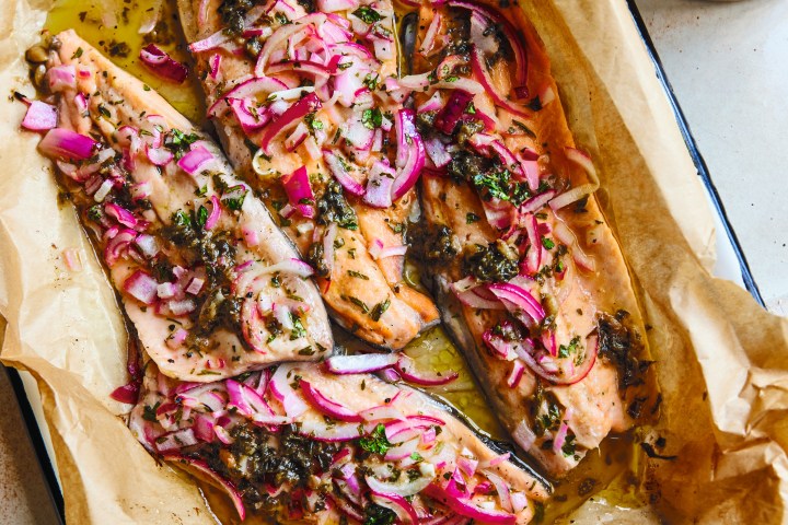 Baked salmon with red onion slices and herbs on parchment paper in a baking dish.