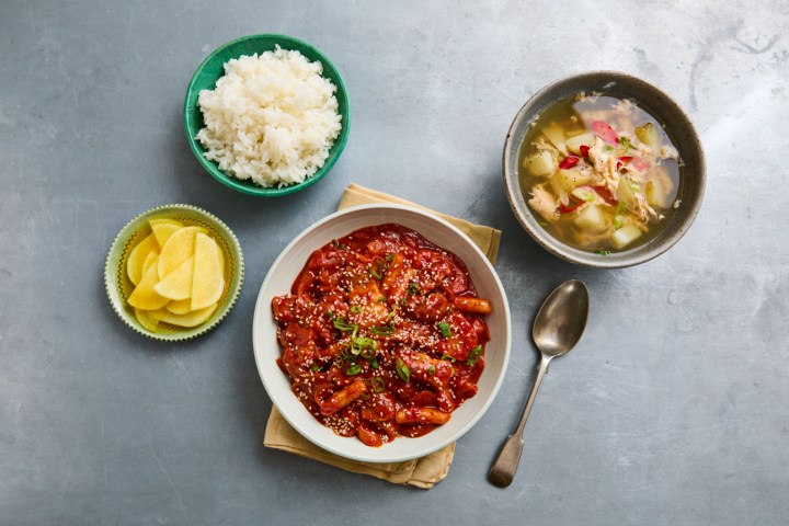 Korean meal with spicy stew, rice, soup, and pickled radish on a gray table.