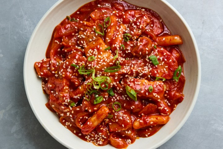 Bowl of spicy Korean rice cakes with sesame seeds and greens on top.