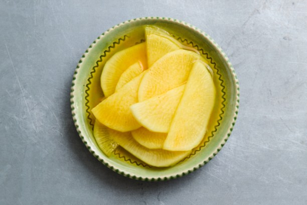 Plate of sliced yellow pickled radish on gray surface.