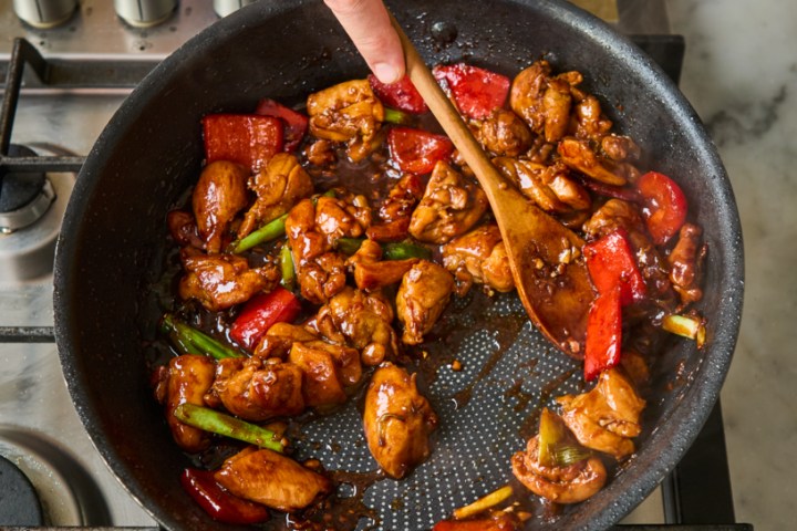 Person cooking stir fry with vegetables in a skillet on the stove.