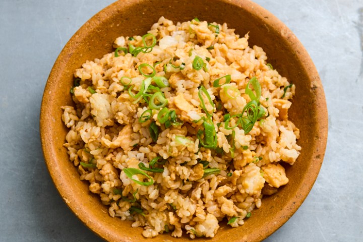 Brown bowl of fried rice with green onions on gray surface.
