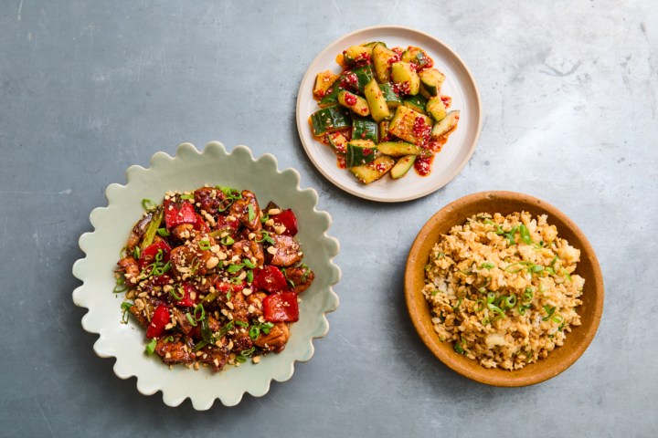Three dishes: stir-fried beef and peppers, spicy cucumber salad, and fried rice on a gray surface.