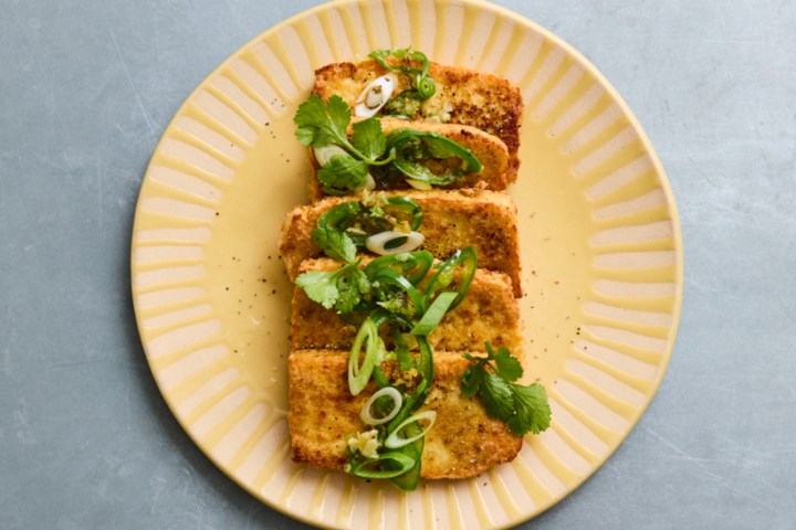 Plate with crispy tofu garnished with green onions and cilantro on a gray background.
