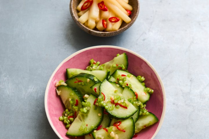 Sliced cucumbers with chili in pink bowl, small bowl with pickled vegetables.