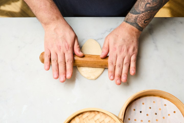 Person rolling dough with a wooden pin on a table.