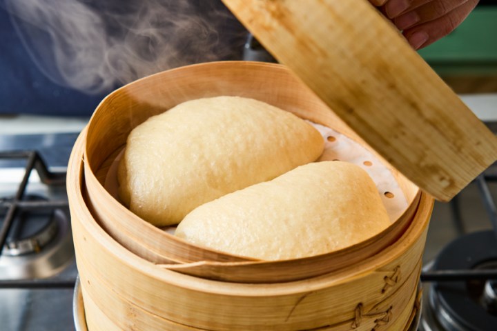 Steaming bamboo basket with buns on a stove.