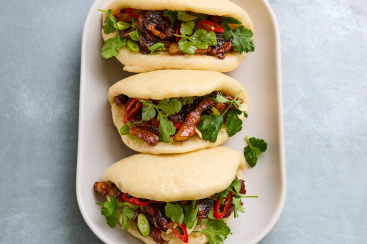 Three bao buns with meat and greens on a white oval plate.