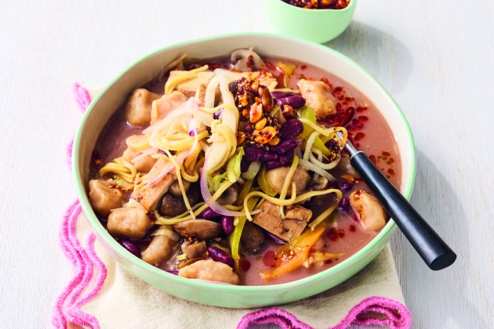 Bowl of noodle soup with vegetables and a side of chili sauce.