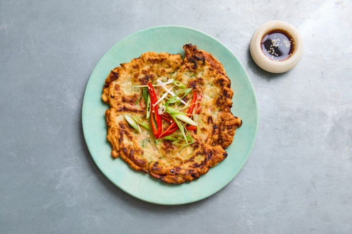 Korean pancake with scallions on a green plate beside a small bowl of sauce.