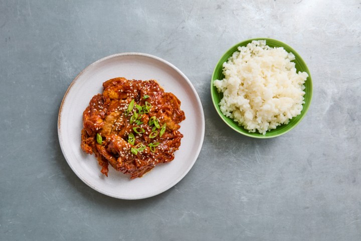 Spicy glazed chicken with green onions on a plate, rice in a bowl.