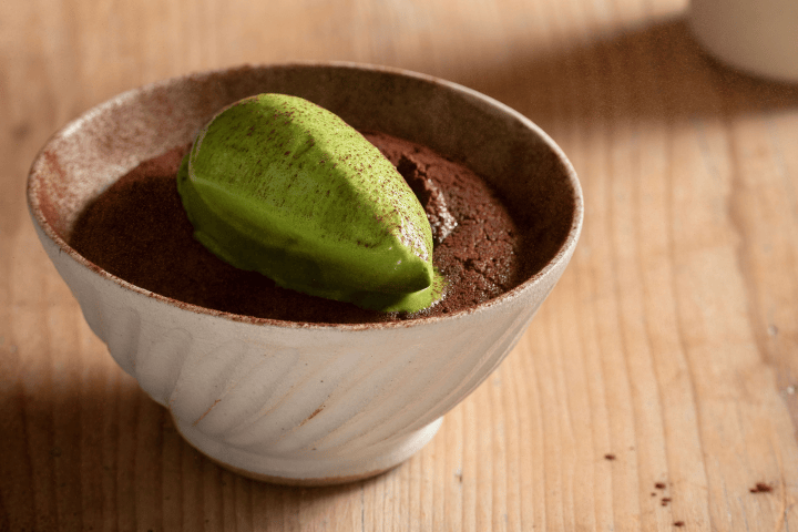 Chocolate dessert with green ice cream in a white bowl on wooden surface.