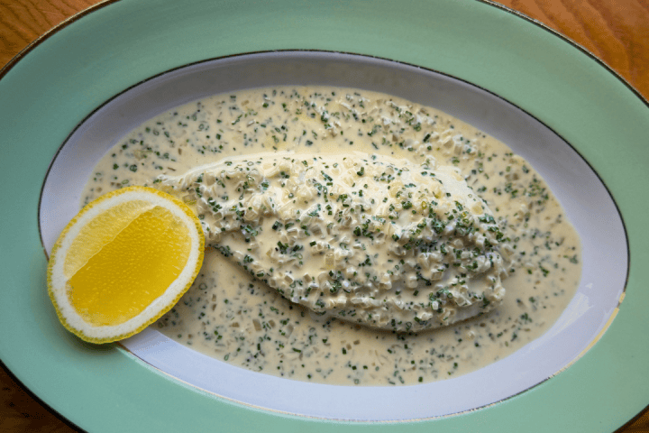 Fish fillet in creamy herb sauce with lemon wedge on green oval plate.